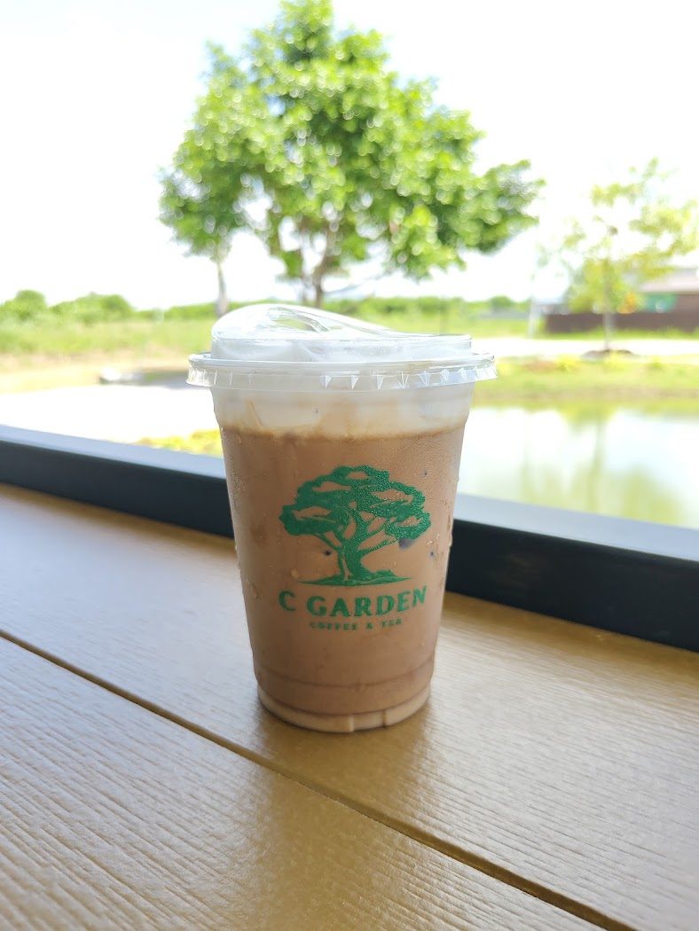 แก้วกาแฟเย็นโลโก้ cGarden วางบนราวไม้ริมสระน้ำ