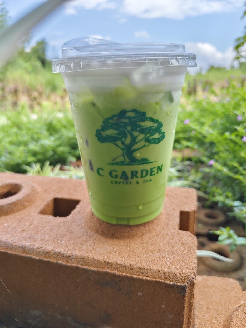 แก้วชาเขียวเย็นพิมพ์โลโก้ต้นไม้ cGarden วางในสวนของร้าน